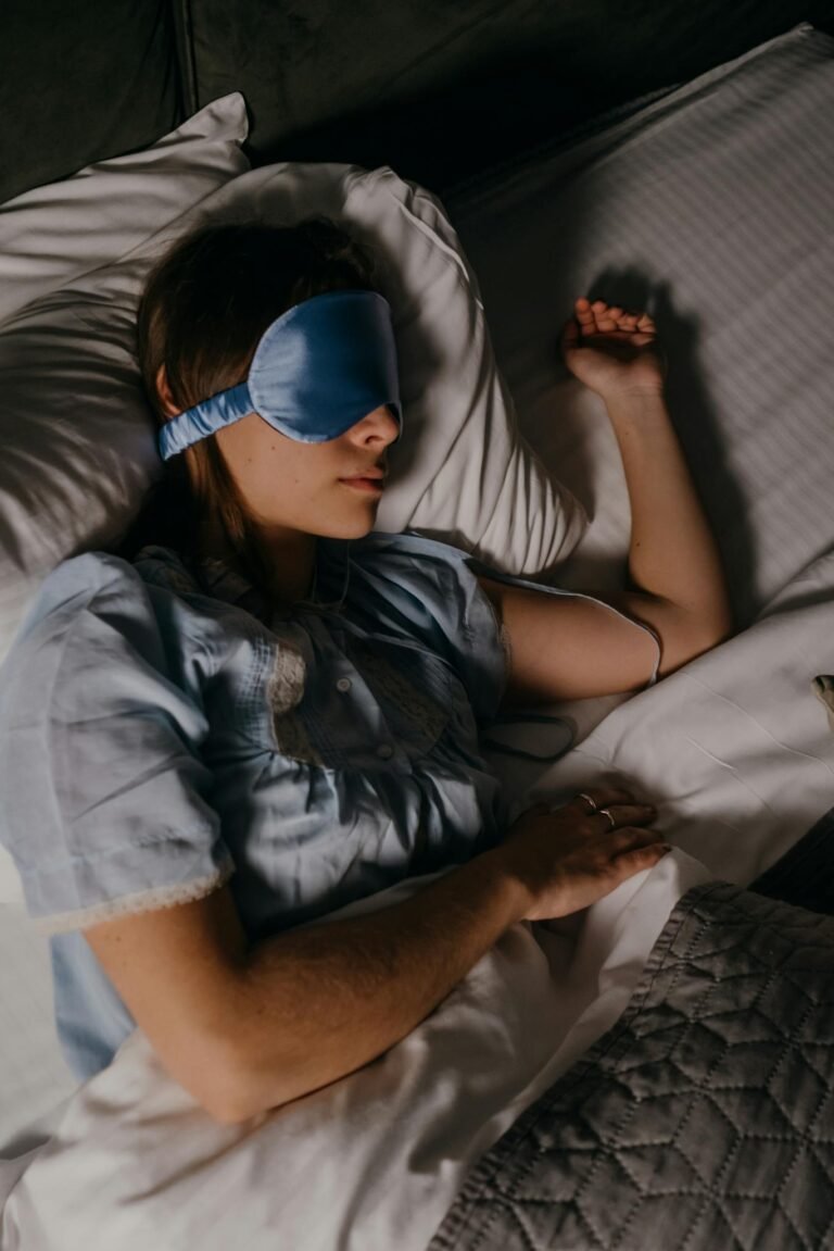 Woman peacefully sleeping with a blue eye mask in a cozy bed setting, promoting restful sleep.